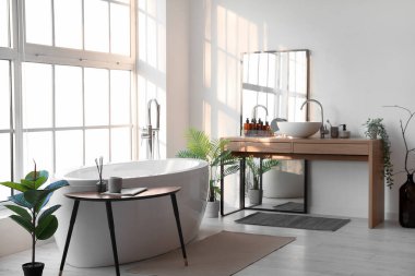 Interior of light bathroom with bathtub, table and mirror