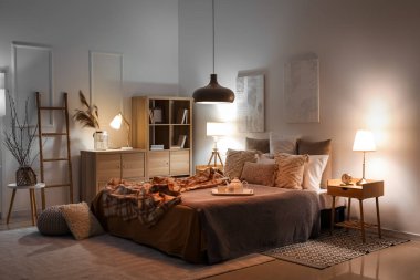 Interior of bedroom with checkered plaid on bed and glowing lamps late in evening