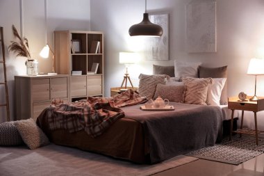 Interior of bedroom with checkered plaid on bed and glowing lamps late in evening