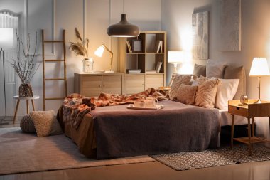 Interior of bedroom with checkered plaid on bed and glowing lamps late in evening