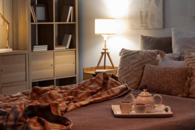 Tray with teapot and cups on bed in dark bedroom