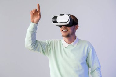 Young man using VR glasses on light background