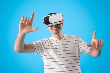 Young man using VR glasses on light blue background
