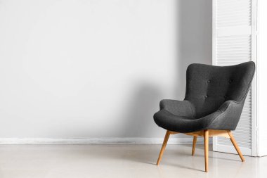 Stylish grey armchair and folding screen near white wall