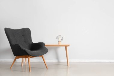 Stylish grey armchair and table with glowing lamp near white wall