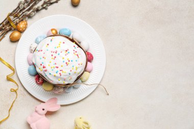 Plate with tasty Easter cake, eggs, bunnies and willow branches on light background