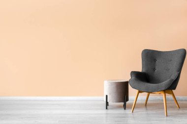Stylish grey armchair and pouf near beige wall