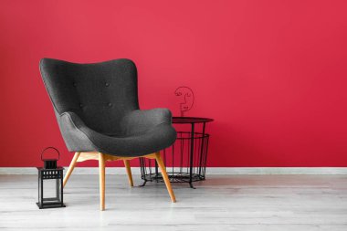 Stylish grey armchair, lantern and end table near red wall