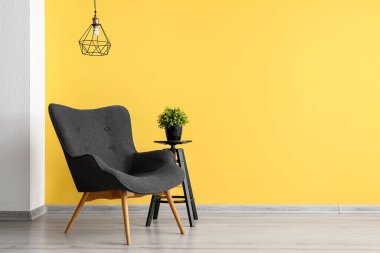 Stylish grey armchair and end table with houseplant near yellow wall