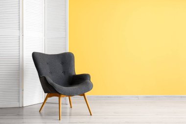 Stylish grey armchair and folding screen near yellow wall
