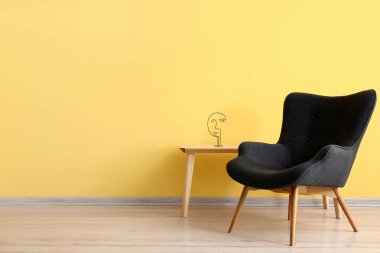 Stylish grey armchair and table near yellow wall