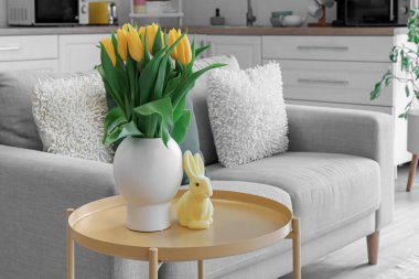Vase with tulips and Easter rabbit on table in kitchen