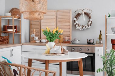 Vase with tulips, basket of Easter eggs and rabbit on dining table in kitchen