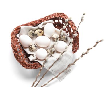 Wicker basket with Easter eggs and willow branches on white background
