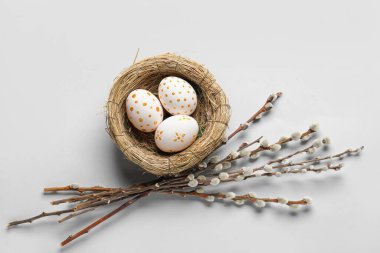 Nest with painted Easter eggs and willow branches on light background
