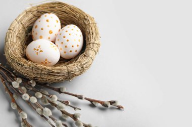 Nest with painted Easter eggs and willow branches on light background