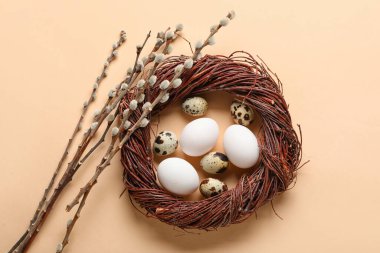Easter eggs, wreath and willow branches on color background