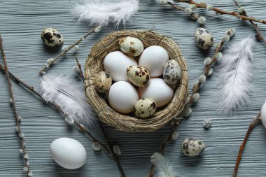 Composition with nest of Easter eggs, feathers and willow branches on grey wooden background