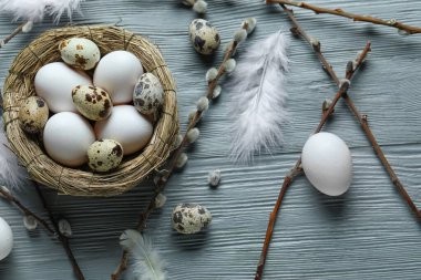 Composition with nest of Easter eggs, feathers and willow branches on grey wooden background