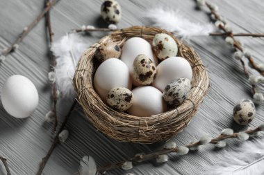Composition with nest of Easter eggs, feathers and willow branches on grey wooden background