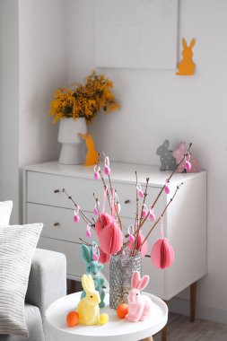 Vase with tree branches, Easter eggs and rabbits on table in living room