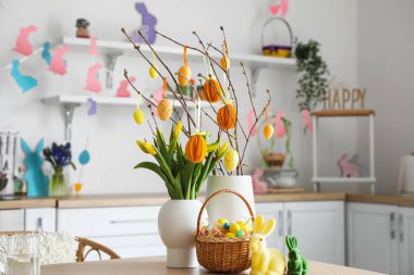 Vases with tree branches, Easter eggs, tulips and rabbits on table in kitchen