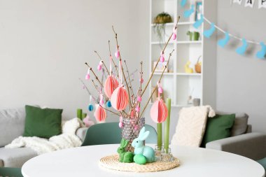 Vase with tree branches, Easter eggs, candles and rabbits on table in kitchen