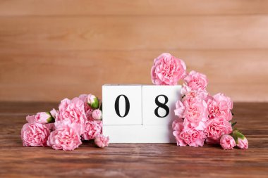Cube calendar with date MARCH 8 and beautiful carnation flowers on wooden table. Women's Day celebration