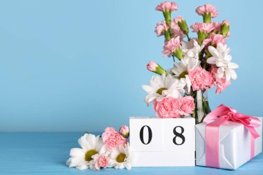 Cube calendar with date MARCH 8, beautiful flowers and gift box on blue wooden table. Women's Day celebration