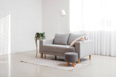 Interior of living room with grey couch, pouf and lamp