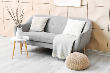 Interior of living room with grey couch and willow branches in vase