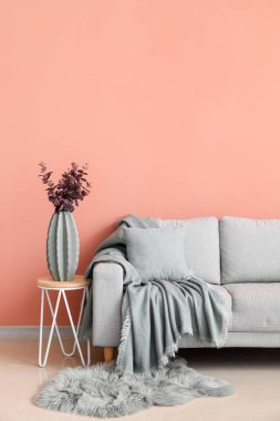 Vase with eucalyptus on table and grey sofa near pink wall