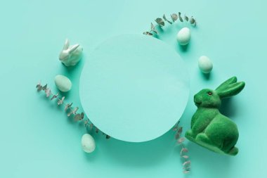 Blank greeting card, painted eggs, Easter bunnies and eucalyptus branches on turquoise background
