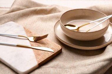 Board and bowl with set of cutlery on grey tablecloth