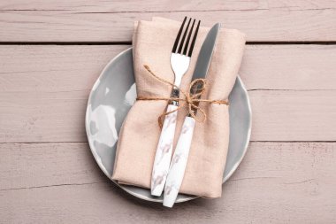 Plate with napkin, fork and knife on white wooden background
