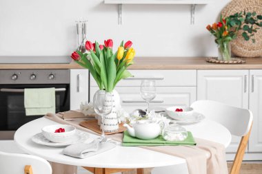 Table setting for International Women's Day celebration with tulip flowers and teapot in interior of room