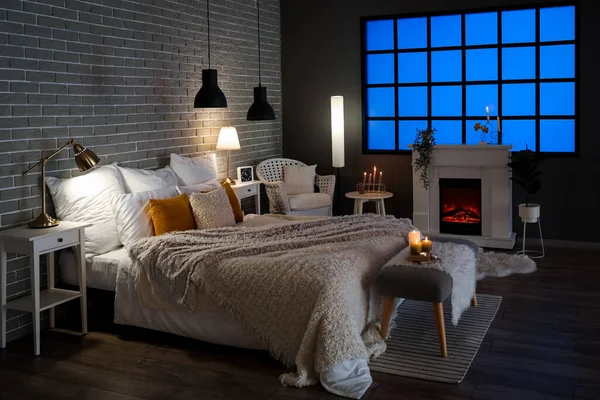 Interior of bedroom with cozy blankets on bed and burning candles at night