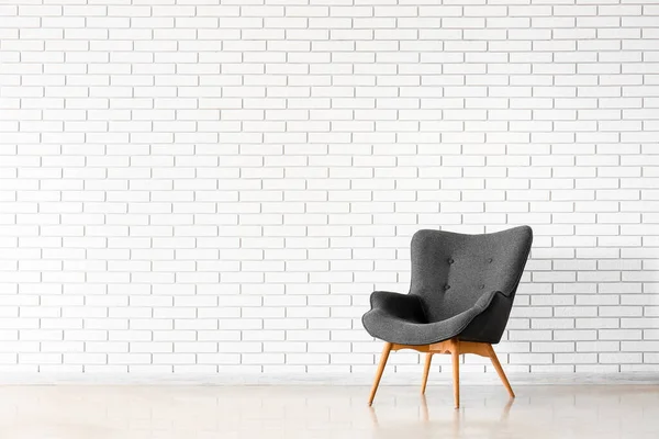 Stylish grey armchair near white brick wall