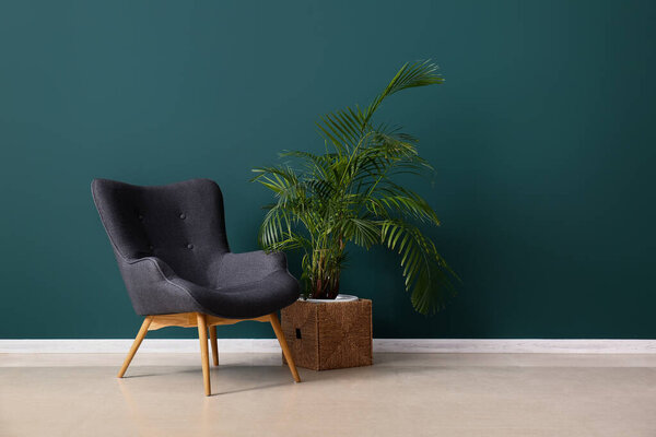 Стильное серое кресло и домашнее растение у зеленой стены