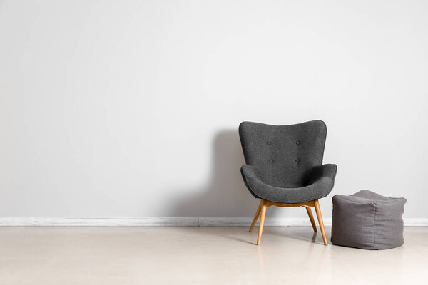 Стильное серое кресло и пуф у белой стены