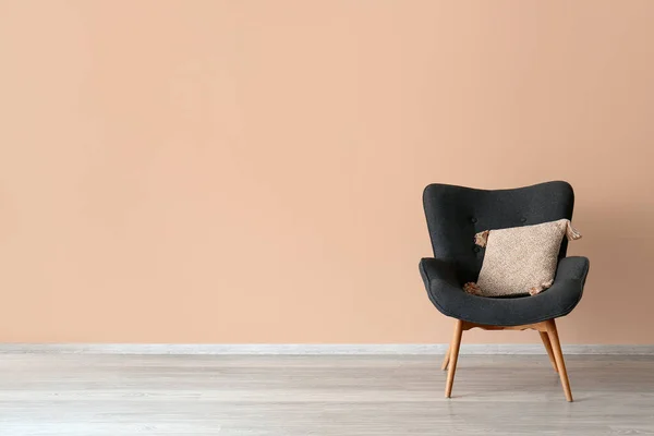 Stylish grey armchair with cushion near beige wall