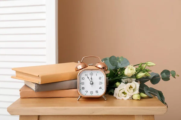Bouquet of beautiful flowers, books and alarm clock on wooden table near color wall