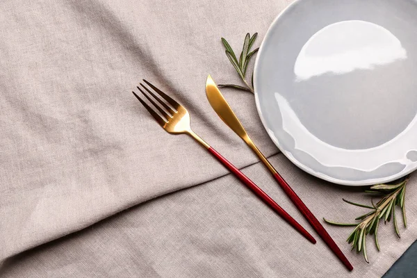 Fork, knife, plate and rosemary on grey tablecloth
