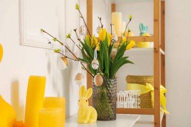 Vase with tulips, tree branches, Easter eggs, candles and rabbit on table in living room