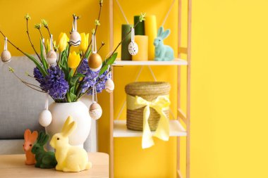 Vase with flowers, tree branches, Easter eggs and rabbits on table in living room