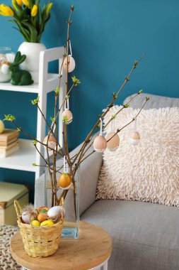 Vase with tree branches, Easter eggs and basket on table in living room