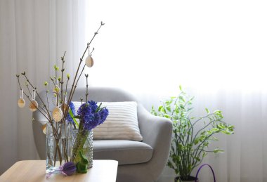 Vases with flowers, tree branches, Easter eggs and rabbit on table in living room