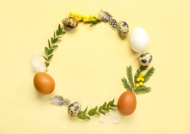 Frame made of Easter eggs, mimosa flowers and eucalyptus branches on yellow background