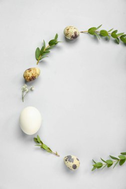 Frame made of Easter eggs and eucalyptus branches on grey background