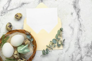 Envelope with blank greeting card, Easter eggs, bunny and eucalyptus branches on white marble background